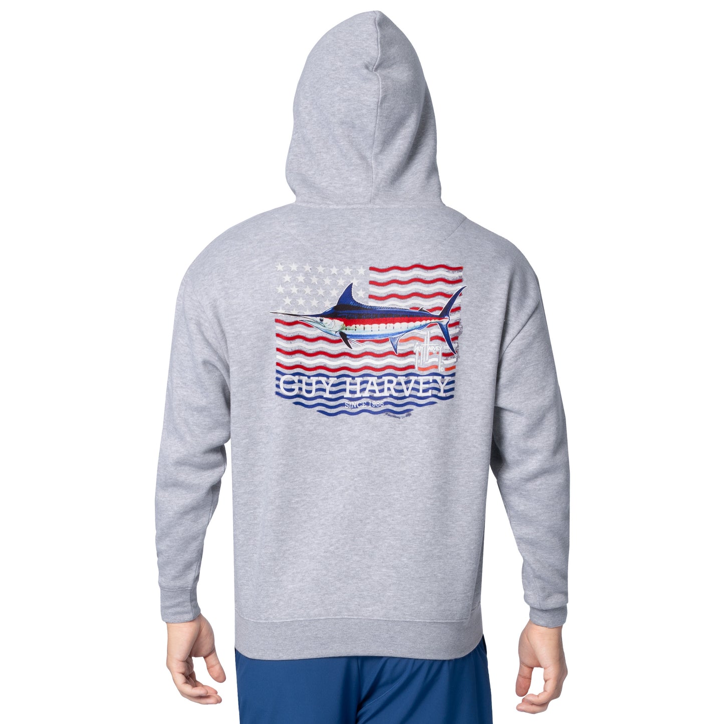 Back view of a man wearing a light gray Guy Harvey fishing fleece hoodie featuring a marlin and American flag artwork.