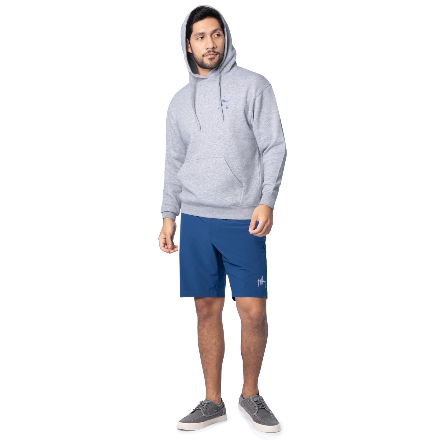 Full-body view of a man wearing a light gray Guy Harvey fishing fleece hoodie with hood up and navy shorts