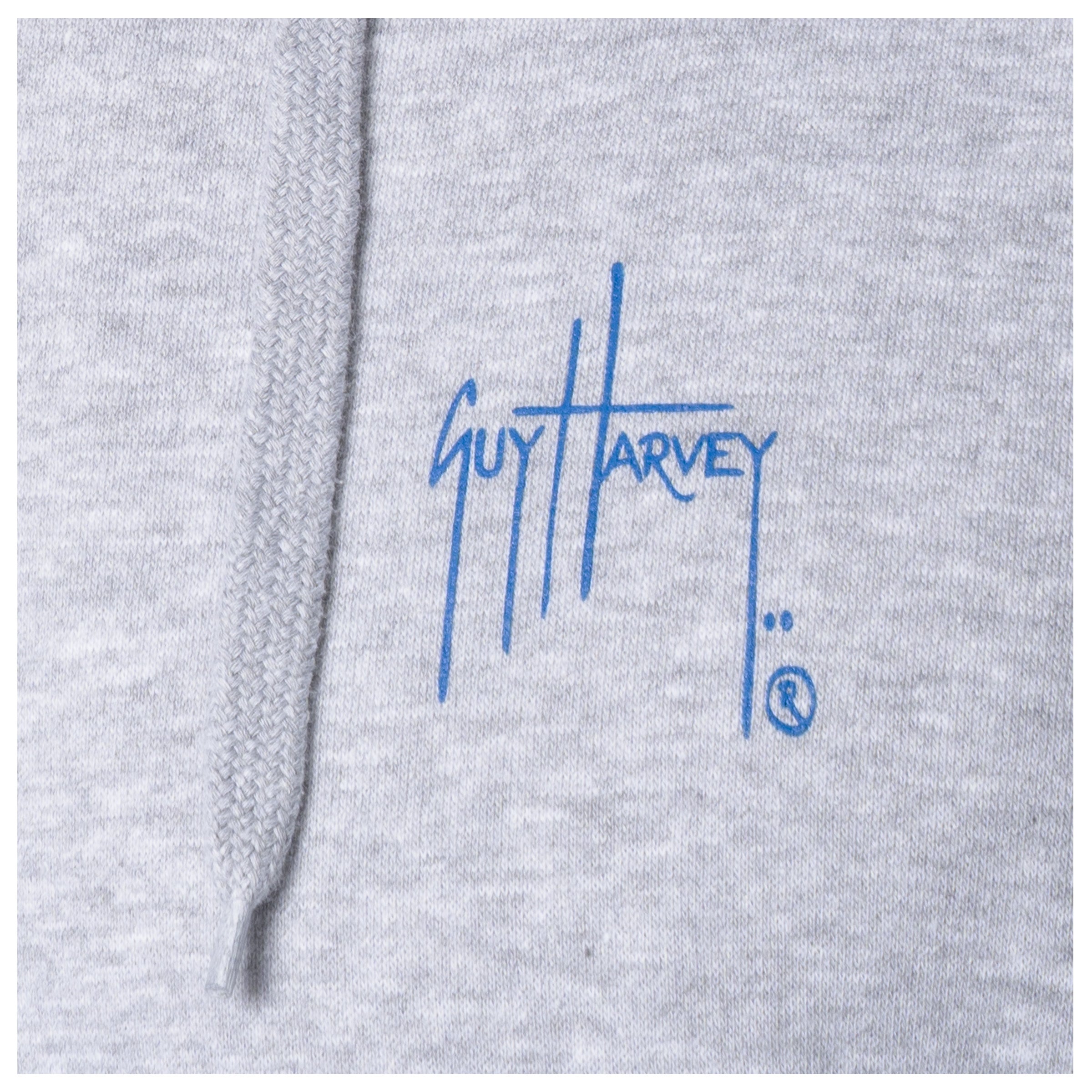 Macro close-up of the printed Guy Harvey signature logo on the fabric of a light gray fishing fleece hoodie.