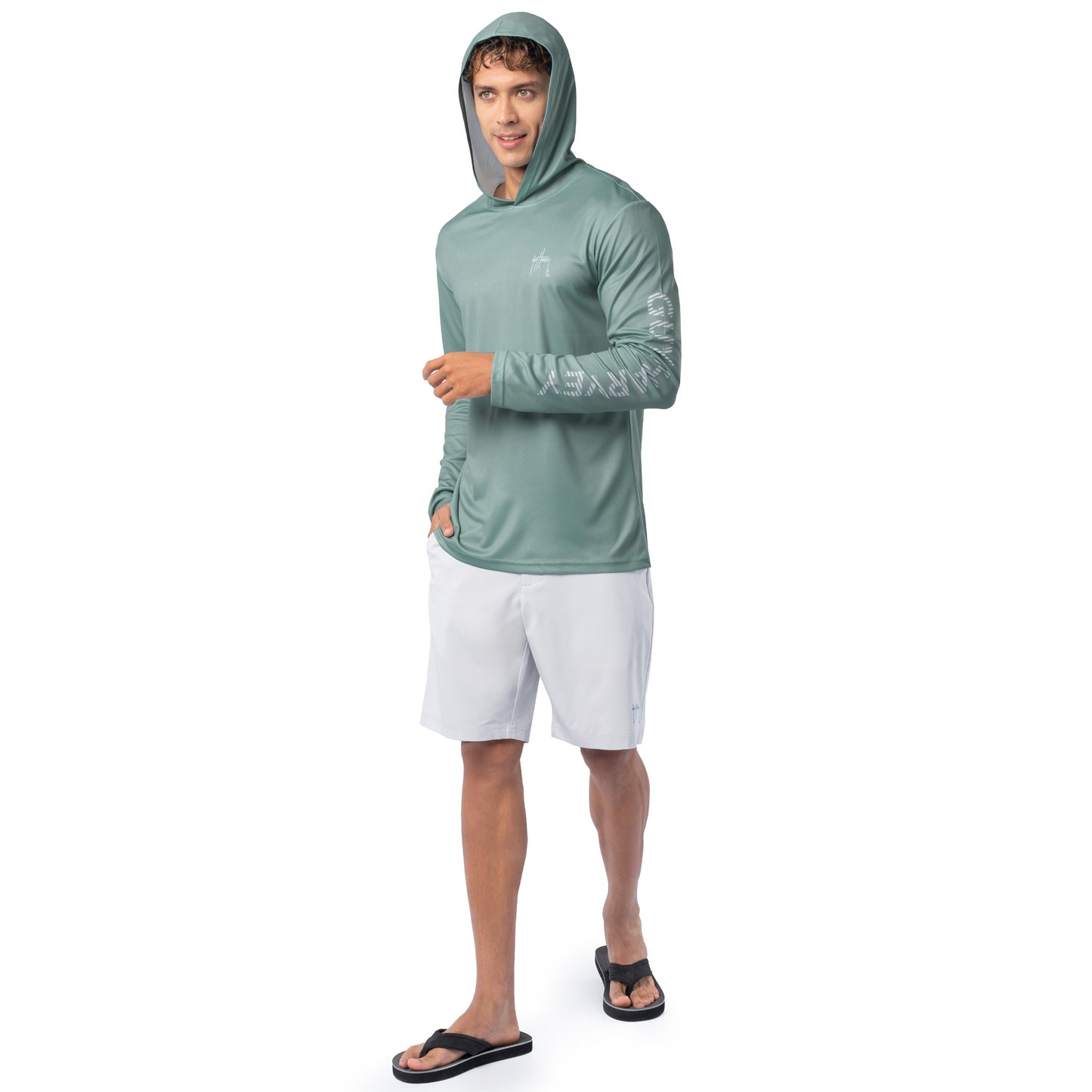Lifestyle image of model wearing seafoam green Guy Harvey Men’s Mahi Gear Sun Protection Hoodie with hood up and white shorts.