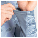 Close-up of a person's hands stretching the elastic cuff of a light blue camouflage long-sleeve shirt to demonstrate its stretch, showing both the patterned fabric and the breathable mesh lining.
