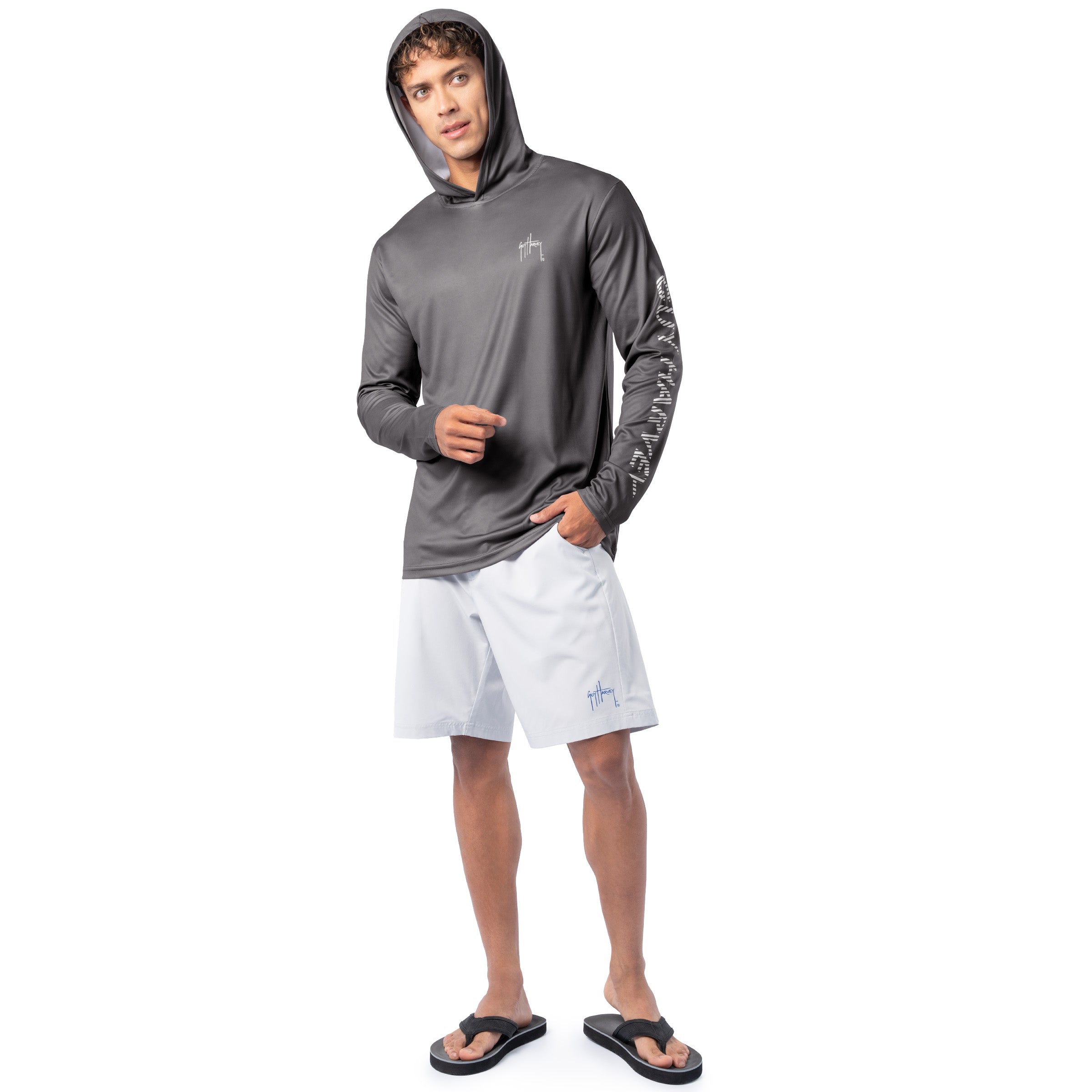 Lifestyle image of model wearing charcoal gray Guy Harvey Men’s Rack Sun Protection Hoodie with hood up and white shorts.