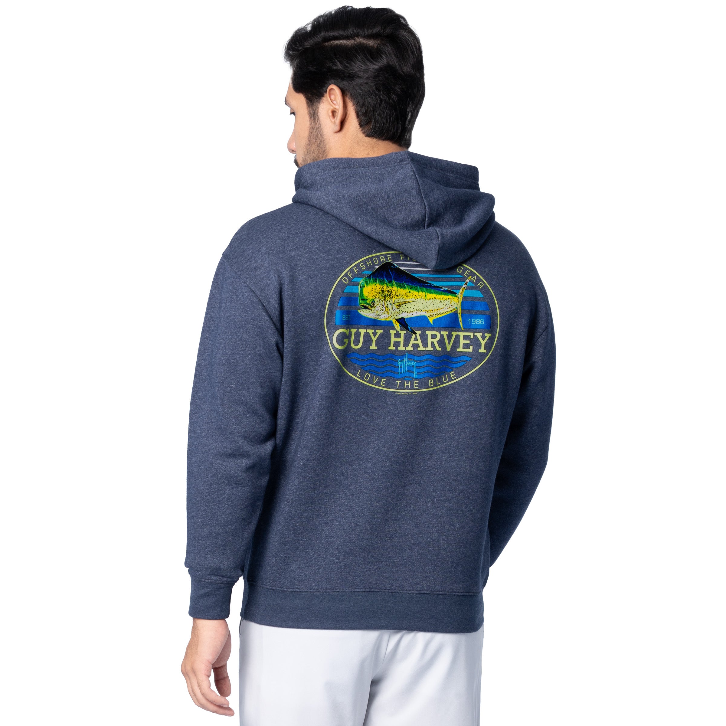 Rear angled view of a man wearing a navy blue Guy Harvey fishing fleece hoodie featuring mahi mahi design and logo text.