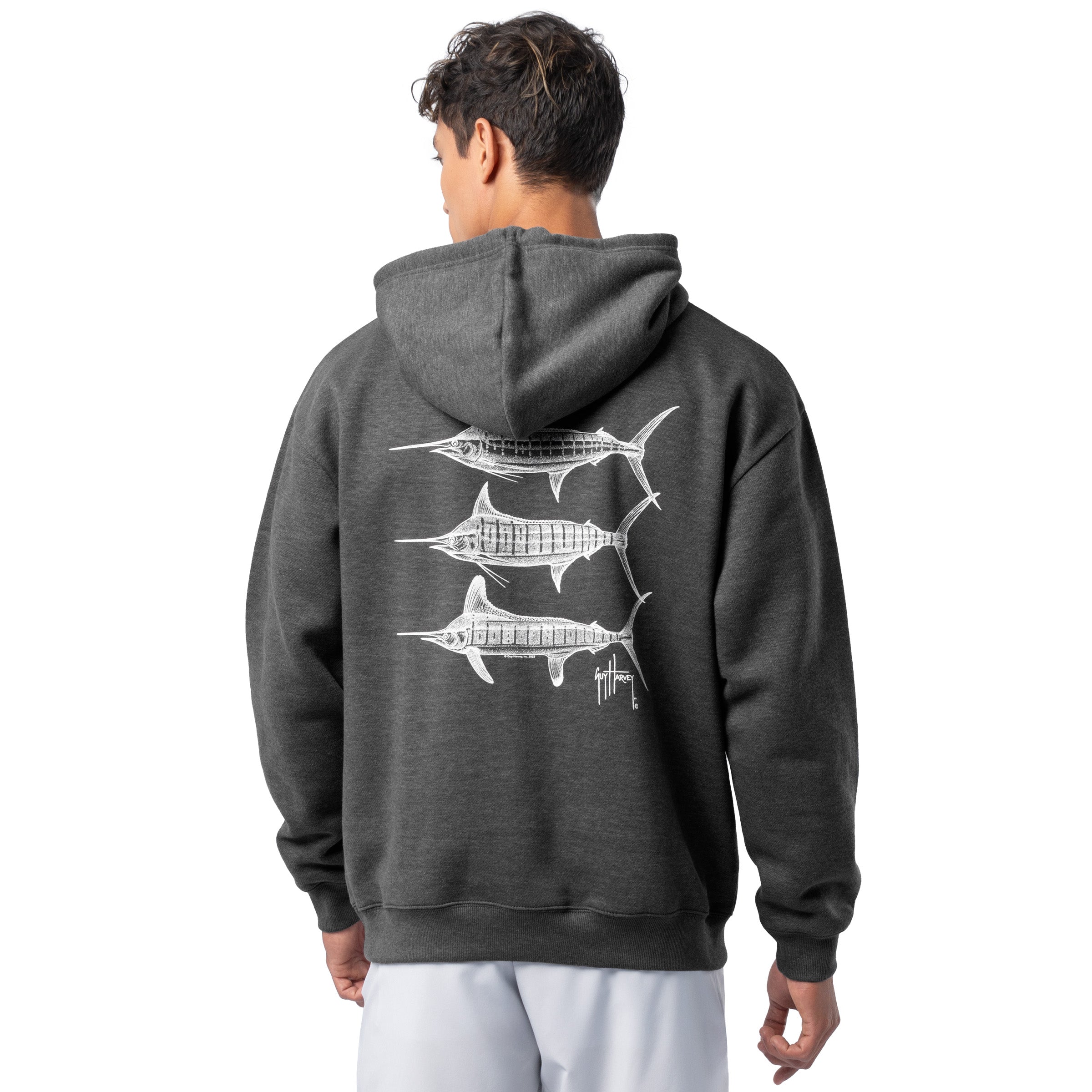 Rear view of a man wearing a dark gray Guy Harvey fishing fleece hoodie featuring three white marlin illustrations on the back.