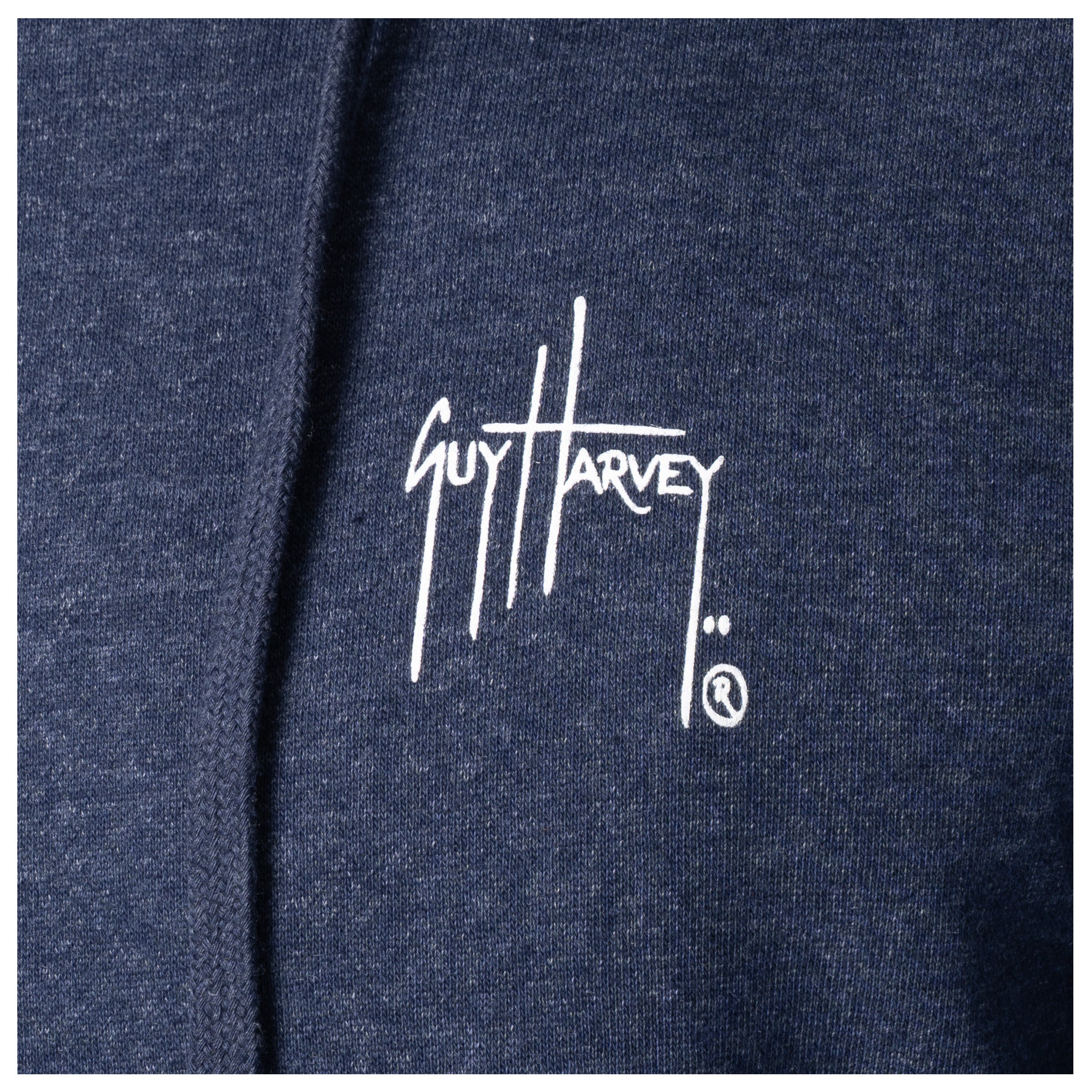 Macro close-up of the printed Guy Harvey signature logo on the fabric of a navy blue fishing fleece hoodie.