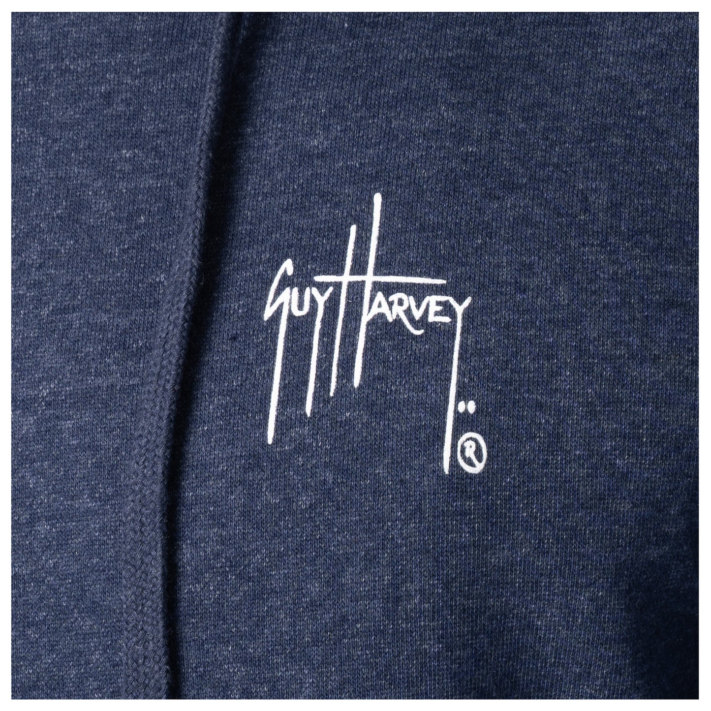 Macro close-up of the printed Guy Harvey signature logo on the fabric of a navy blue fishing fleece hoodie.