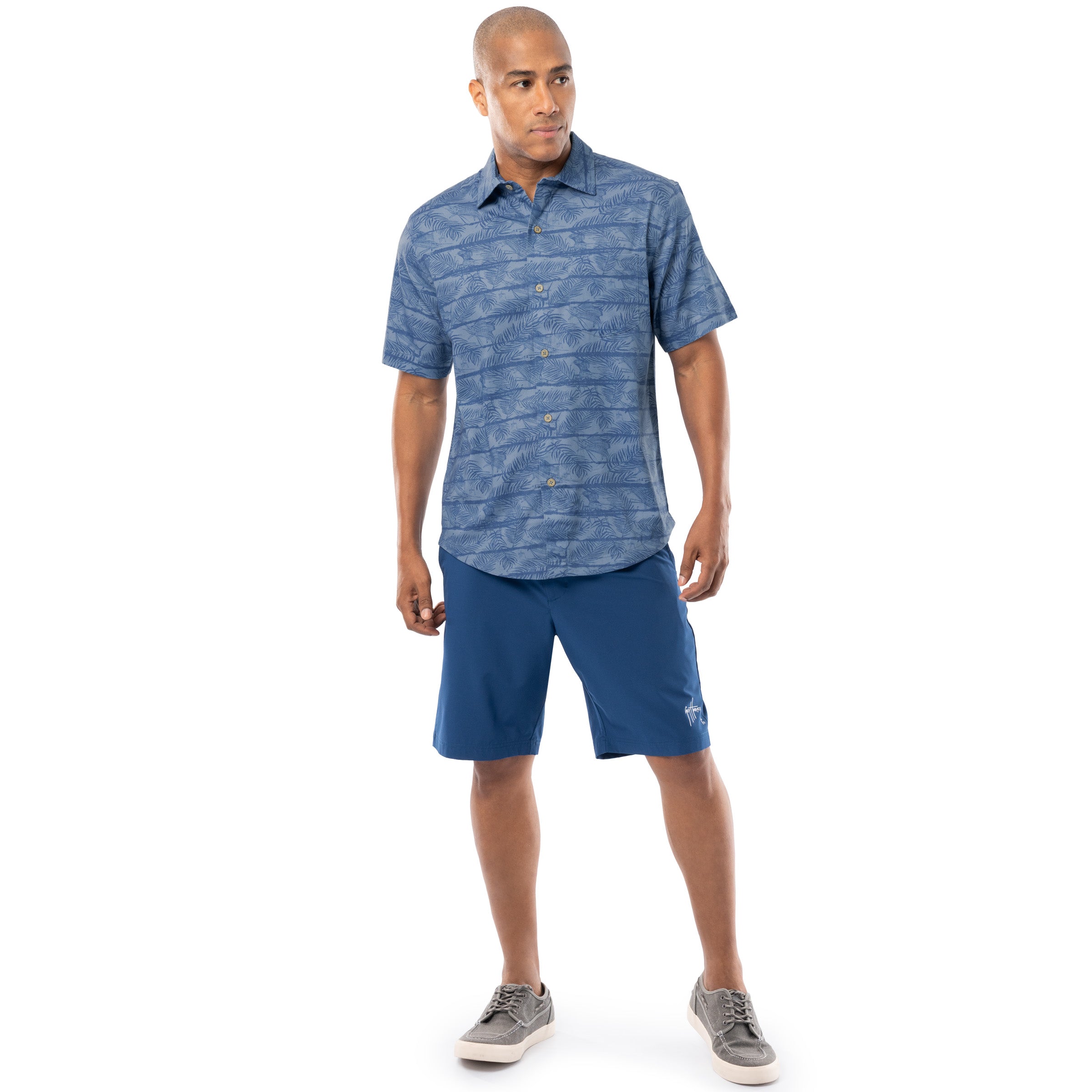 Lifestyle image of model wearing denim blue Guy Harvey Men’s Sandbar Printed Resort Shirt with blue shorts.