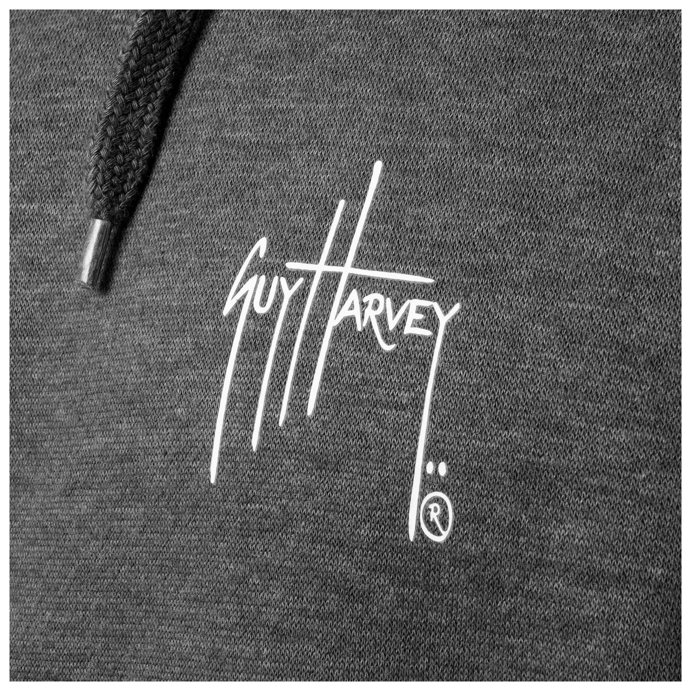 Close-up of the white Guy Harvey logo printed on the chest of a dark gray fishing fleece hoodie.