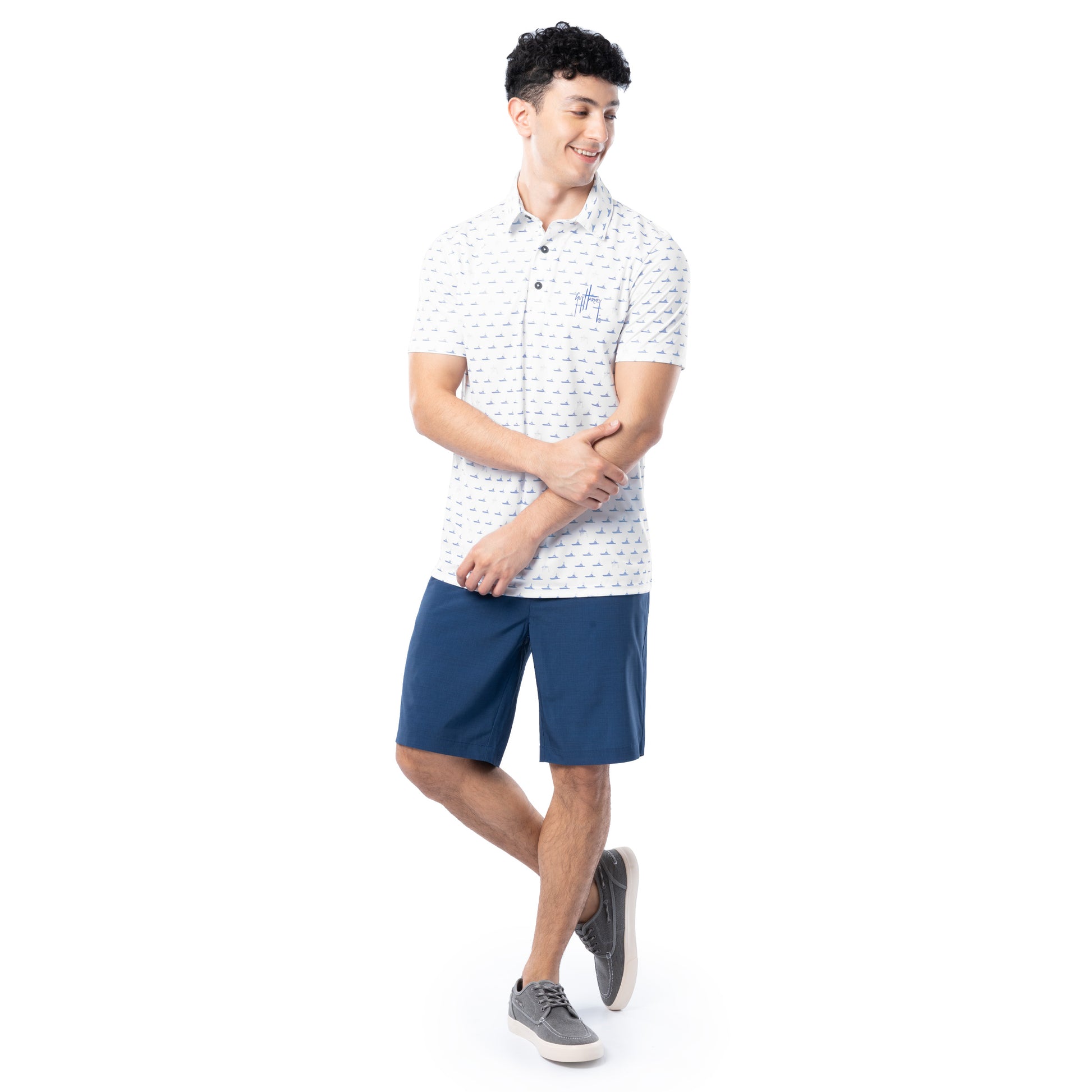 Lifestyle image of model wearing white Guy Harvey Men’s White Fleet Printed Polo Shirt with navy shorts.