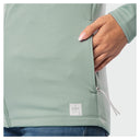 Close-up of a woman wearing a blue surf zippered jacket, showing a hand with pink manicured nails reaching into the side pocket. A small white square Guy Harvey logo patch is visible near the bottom hem.