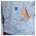 Close-up of a light blue and white camouflage hoodie with a front pocket and a small blue Guy Harvey logo patch, shown on a person with one hand in the pocket.