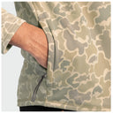 Close-up of a person wearing a camouflage zip-up hoodie with a side pocket and drawstring, showing the arm and torso against a light gray background.