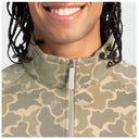 Close-up of a person wearing a camouflage zip-up jacket with a high collar and a visible Guy Harvey logo on the chest.