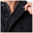 Close-up of a black hooded jacket with a partially unzipped collar, metal snap buttons, and drawstrings, shown on a model with a hand adjusting the collar.