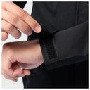 Close-up of a person's hands fastening a black sleeve with a hook-and-loop strap onto a black jacket or uniform.