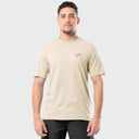 Man wearing a beige t-shirt with a small Guy Harvey logo on a light gray background