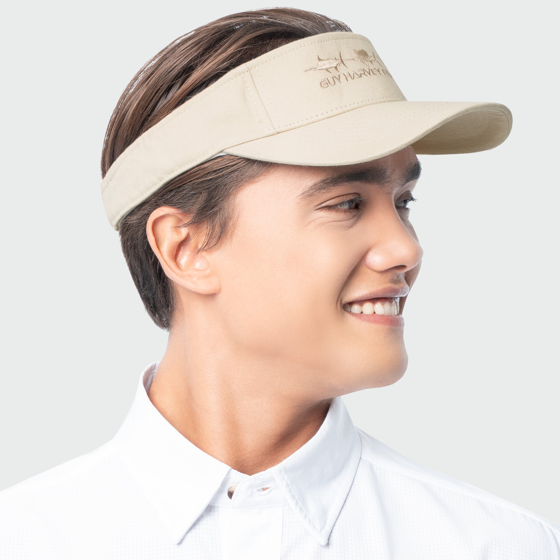 Person wearing a beige visor with a embroidered billfish on a light gray background