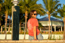 Person in a red shirt sitting on a ledge with palm trees in the background