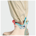 Close-up of a person's lower legs and feet wearing beige fishing pants and beige waterproof deck boots with turquoise, coral, and mint green accents, set against a plain light gray background.