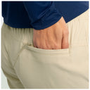 Close-up of a person wearing beige drawstring fishing pants and a navy long-sleeve top, with the hand reaching into the back pocket.