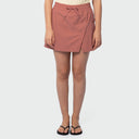A model wearing a dusty rose wrap-style fishing skort with a drawstring waist, paired with black flip-flops, shown against a light gray studio background.
