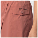 Close-up of dusty rose fishing skort featuring a front flap pocket with the brand name 'GUY HARVEY' printed in black on the tab and a matching fabric button.
