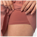 Close-up of a person wearing dusty rose fishing skort, lifting the sides of the fabric to show the inner waistband and skin underneath.