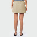 A model from the back wearing a light beige fishing skort with side pockets, paired with black flat sandals and a gray top, against a light gray studio background.