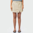A model wearing a light beige wrap-style fishing skort with side technical pockets and a drawstring waist, paired with black flip-flops against a light gray studio background.
