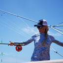 A woman wearing a Guy Harvey Marlin Air sun protection hood in a blue mallard camo while fishing.