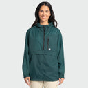 A woman wearing a dark teal green hooded anorak jacket with a front zipper and a zippered chest pocket, paired with light beige pants, against a solid light gray background.