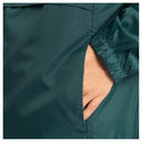 Close-up of a person's hand sliding into a side pocket of dark teal-green outdoor pants, showing the elasticated cuff and fine grid texture of the fabric.