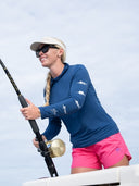 Woman in blue long-sleeve shirt and pink shorts holding a fishing rod on a boat.
