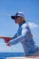 A female angler wearing a blue camo Guy Harvey Marlin air sun protection hood while fishing