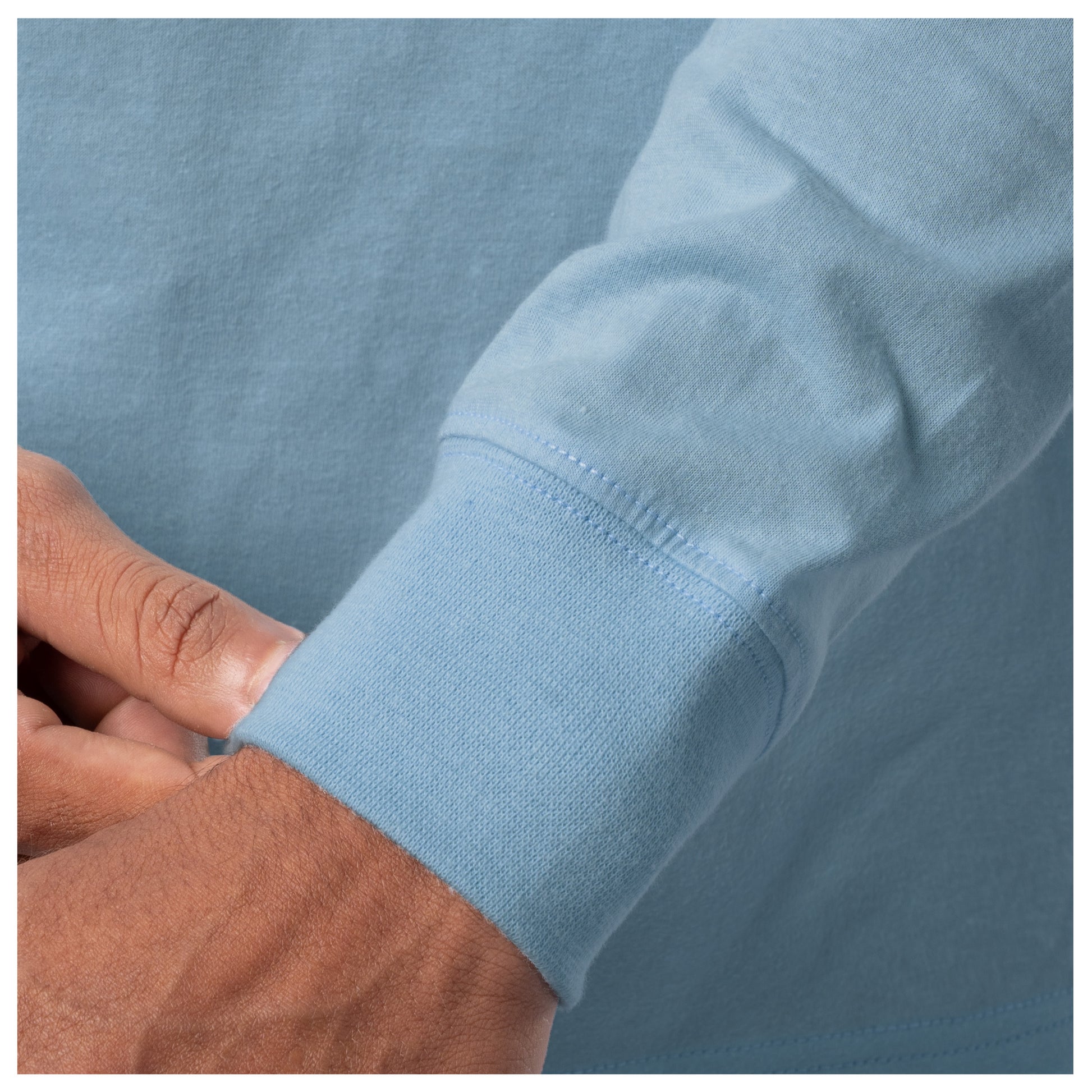 Close-up of a light blue shirt sleeve with a hand adjusting it against a matching background.